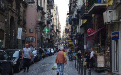 Calle urbana de Nápoles con tránsito peatonal y actividades diversas, ilustración de la porosidad urbana y el flujo de la vida cotidiana en la ciudad.