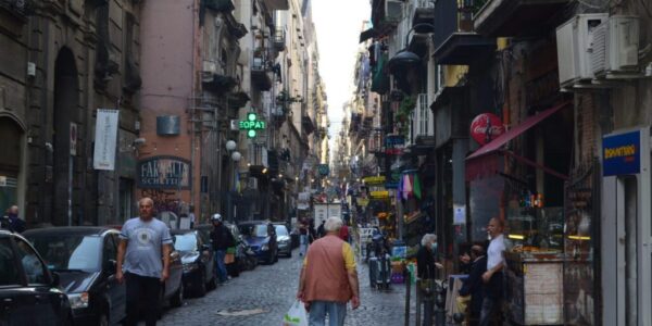 flaneur-porosidad-napoles Calle urbana de Nápoles con tránsito peatonal y actividades diversas, ilustración de la porosidad urbana y el flujo de la vida cotidiana en la ciudad.