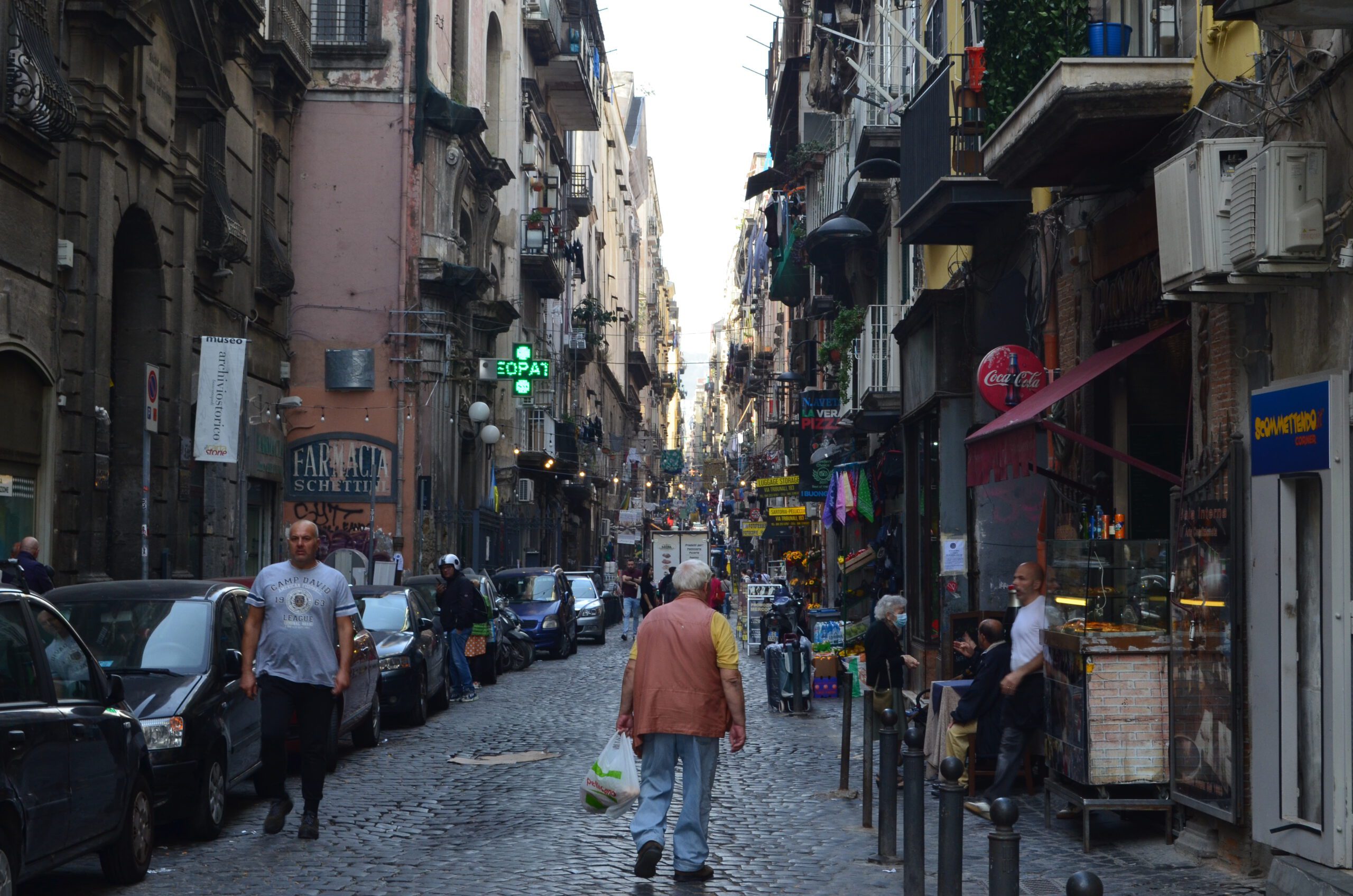 Calle urbana de Nápoles con tránsito peatonal y actividades diversas, ilustración de la porosidad urbana y el flujo de la vida cotidiana en la ciudad.